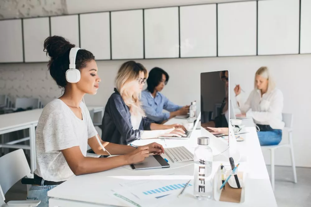 Diverse female developers collaborating on sustainable mobile app development at their workstations.